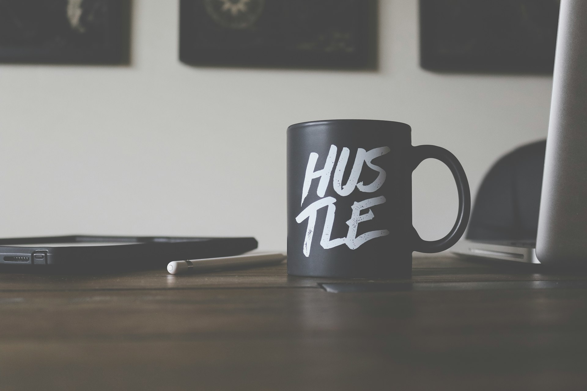 A matte black coffee mug featuring the word 'HUSTLE' in bold, white typography on a workspace background. This motivational design symbolizes the drive and determination essential for success, perfectly complementing the modern professional's desk.